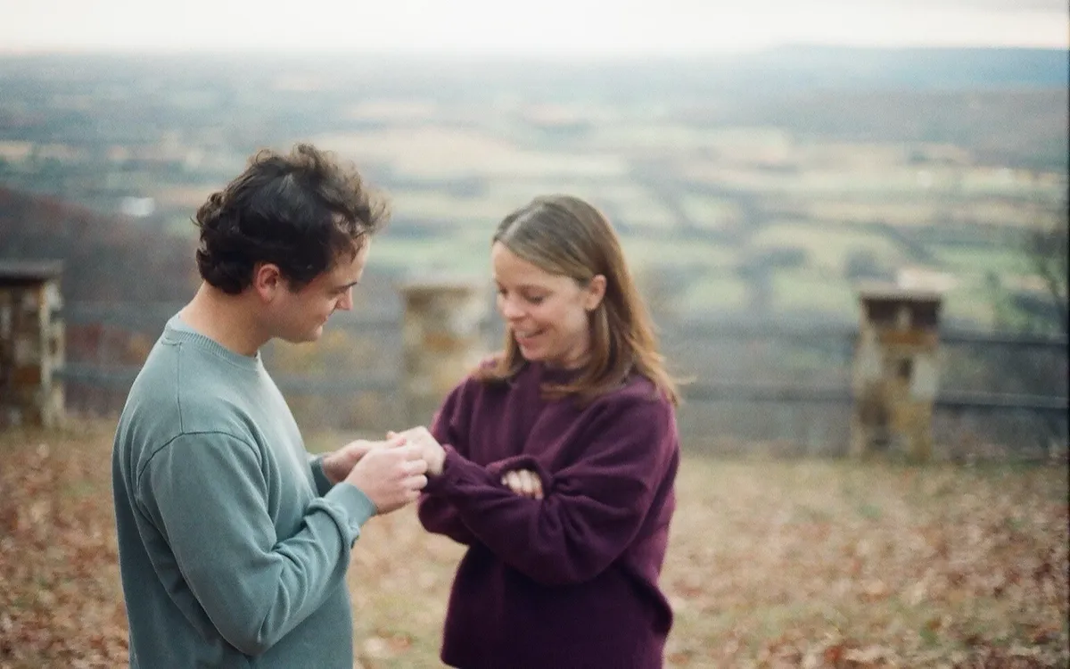 Hobey putting the ring on Shelby's finger at an overlook, valley soft behind